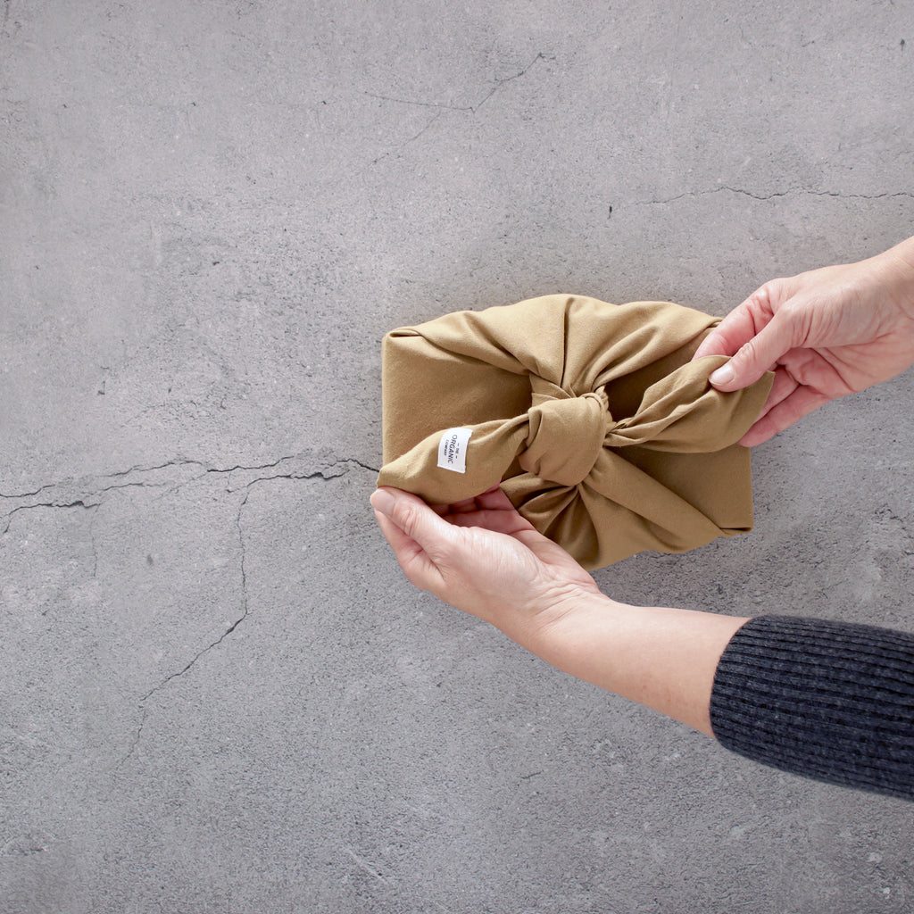 Hands tying a gift wrapped with the tan fabric reusable gift wrap. Concrete background.