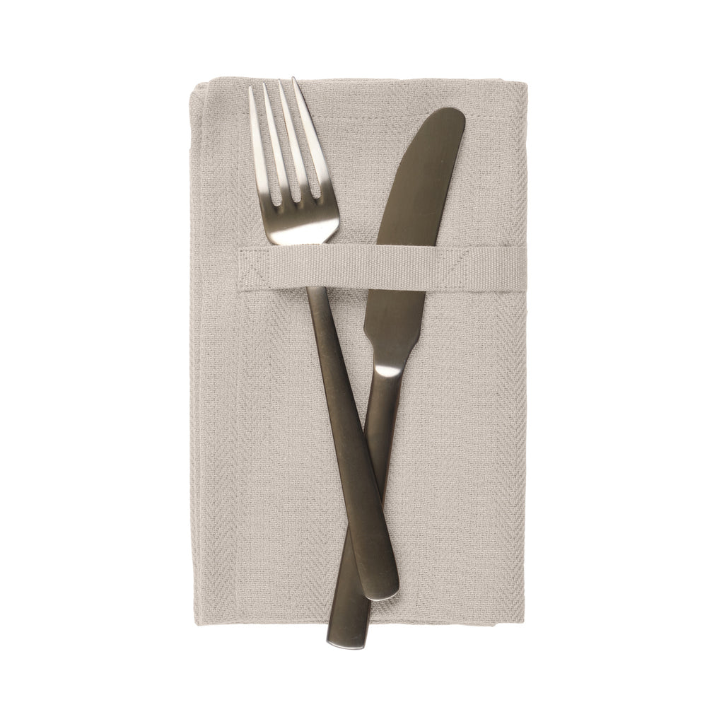 A herringbone weave light tan dinner napkin with a loop holding a fork and knife in place. White background.