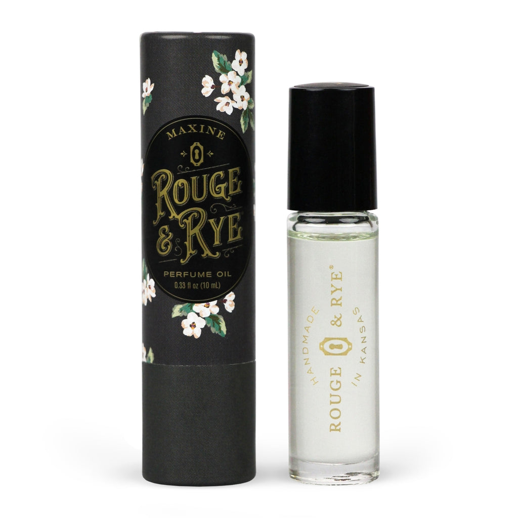 Clear Maxine perfume oil roller in clear glass bottle with black plastic cap next to black floral packaging. White background.