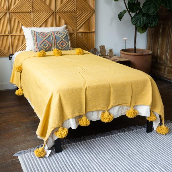 Woven cotton mustard blanket is on twin bed in front of a geometric wood headboard.