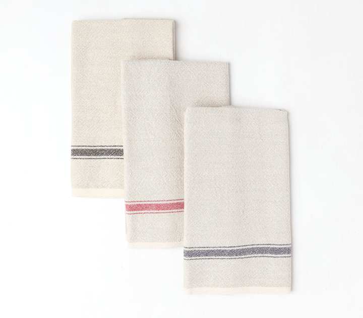 Group of three vintage linen tea towels staggered on top of each other. Natural with black stripe then natural with red stripe then natural with blue stripe.