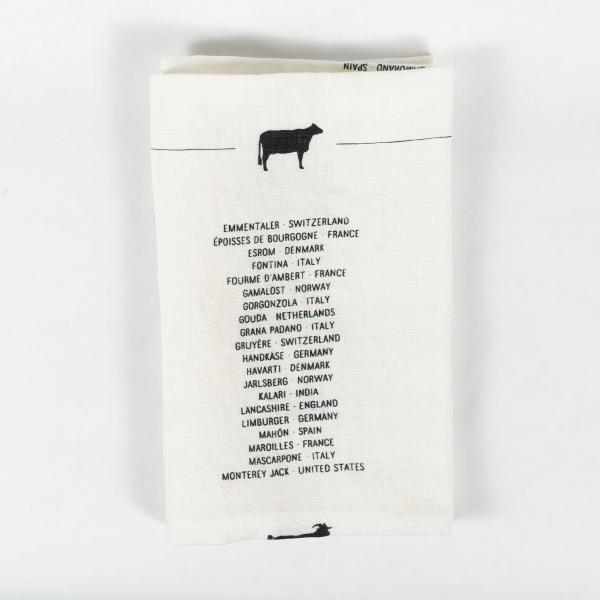 Folded white tea towel with screen printed cow above a list of international cheeses. Black on cream.