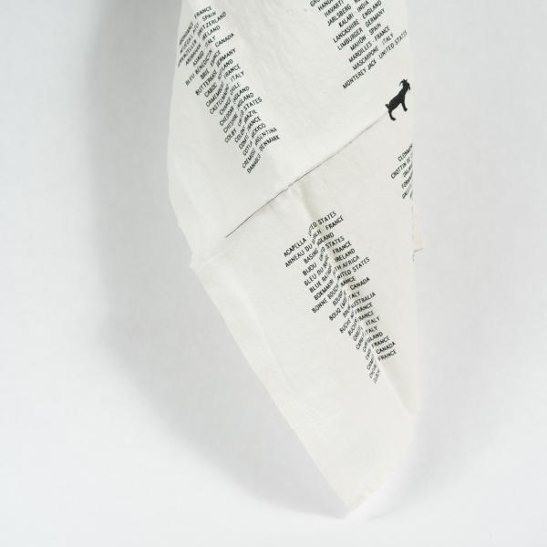 Draped white tea towel with screen printed goat above a list of international cheeses. Black on cream.