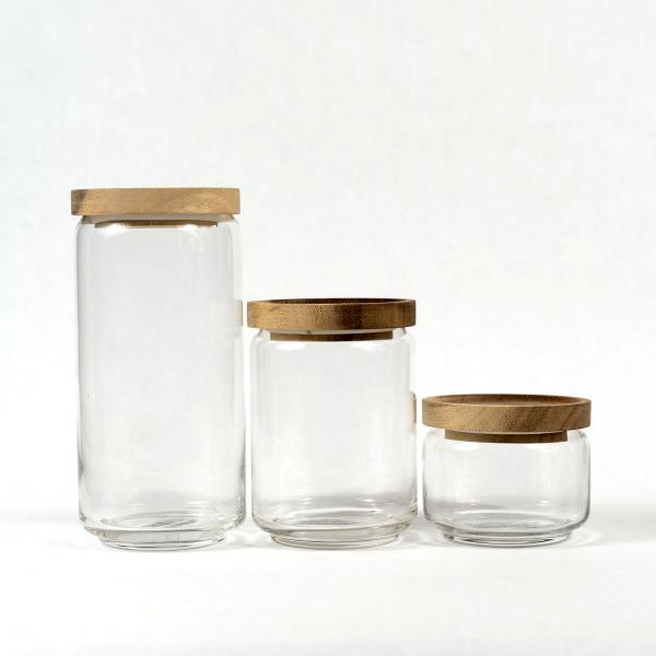 Three sizes of glass jars with acacia wood lids sitting in a row on a white background.
