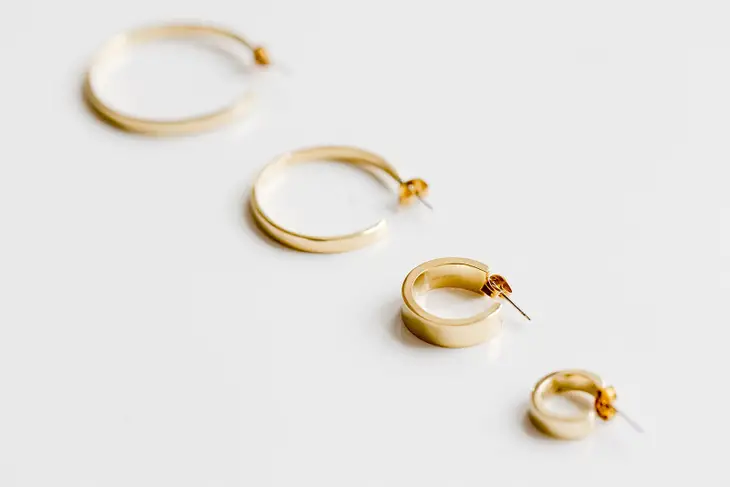 Four different sized gold hoop earrings in a diagonal row on a white background.
