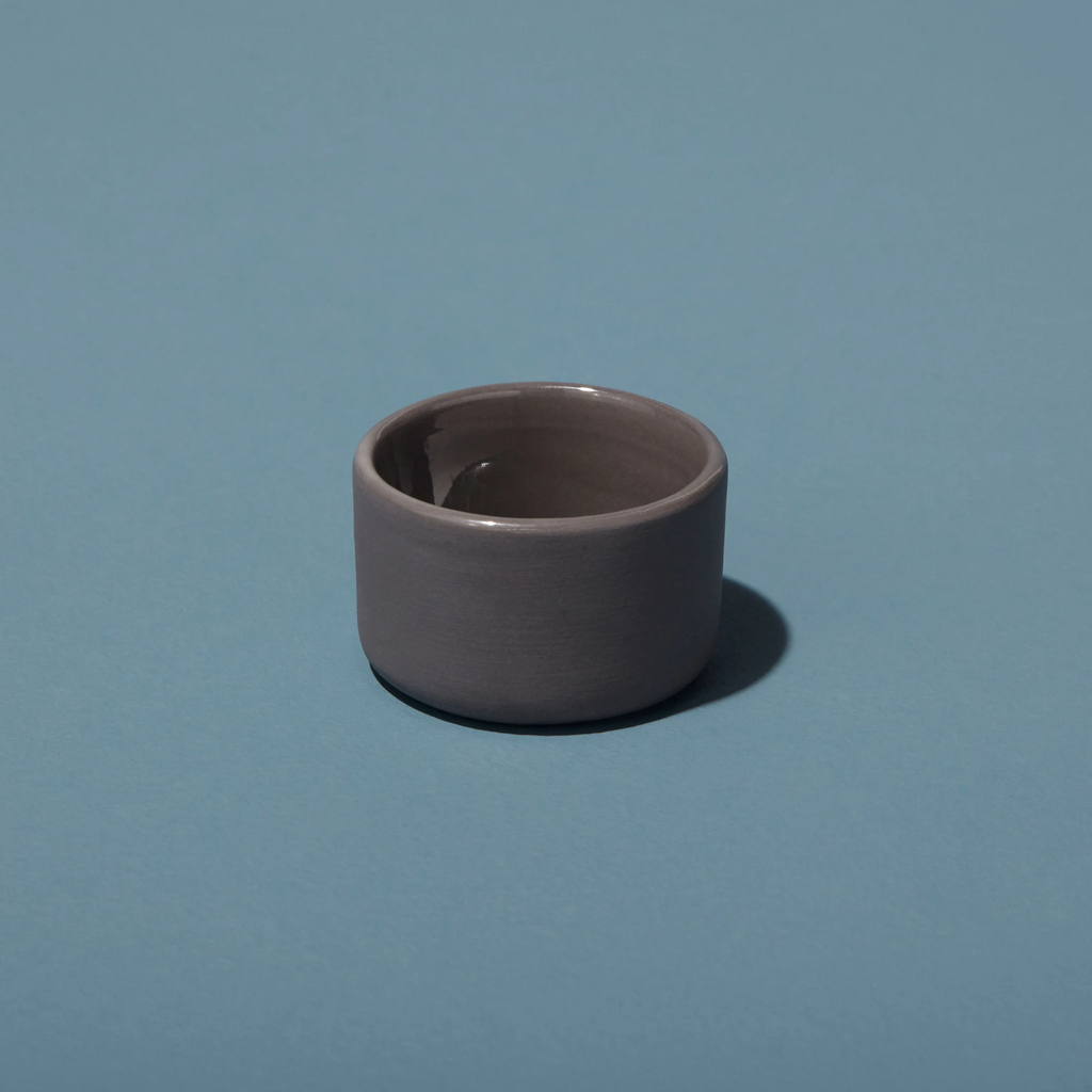 Small dark gray stoneware cellar / bowl on a blue background.
