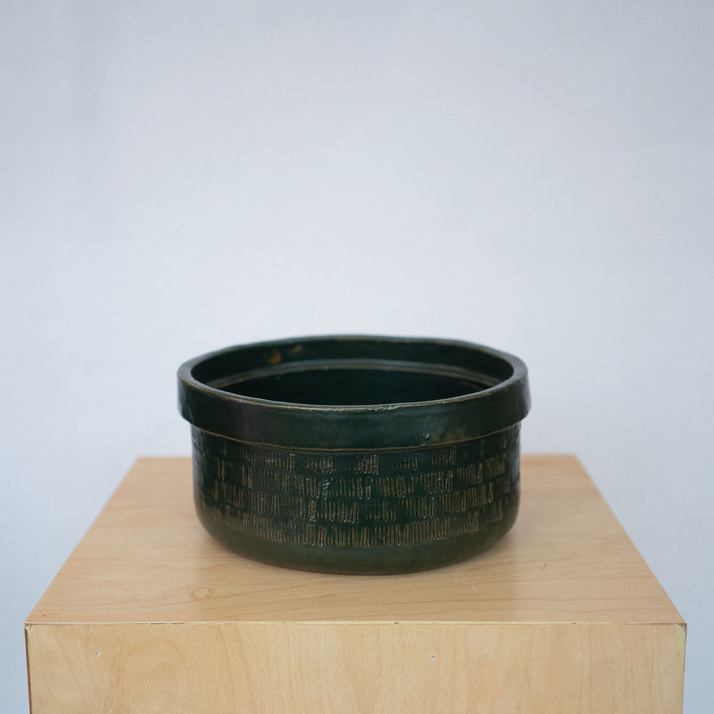 Small dark green ceramic bowl on a wood platform in front of a white background.