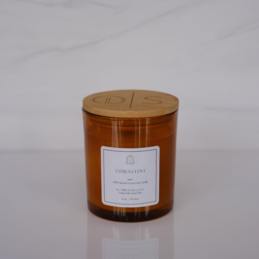 Amber glass candle with a white square label and bamboo lid. Gray background.