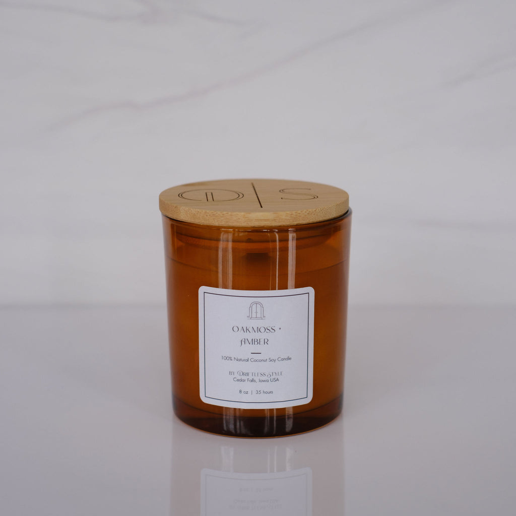 Amber glass candle with a white square label and bamboo lid. Gray background.