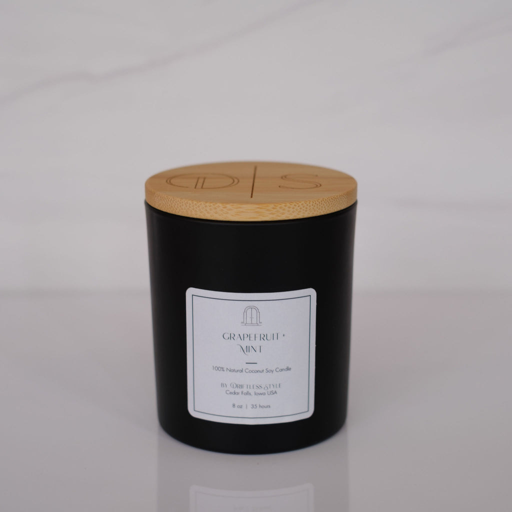 Matte black glass candle with a white square label and bamboo lid. Gray background.