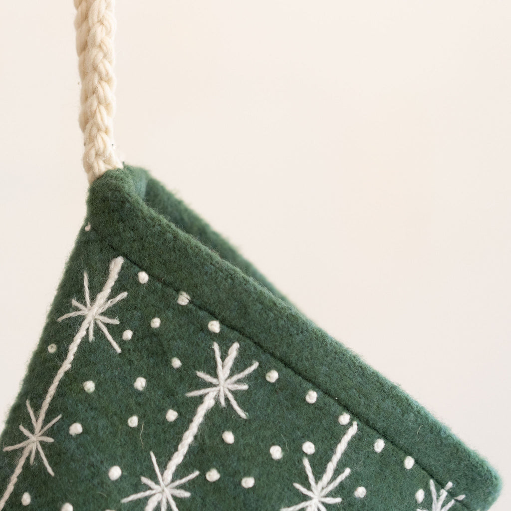 Detail of Green wool stocking with embroidered cream snowflake and polka dot design. Hangs from cream braided hanging loop. 