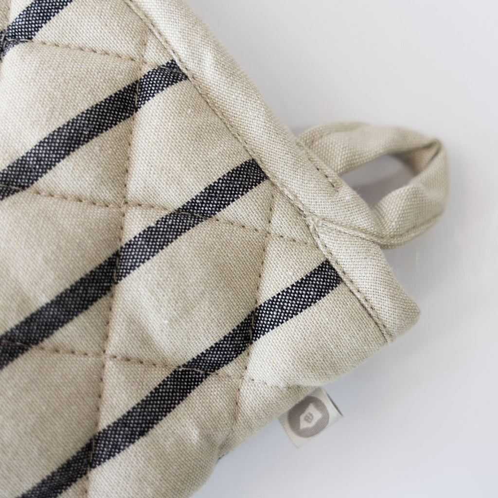 Close up of hanging loop on a Cream oven glove with black stripes on a white background.