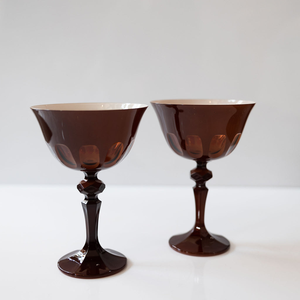 Pair of amber toned tall handblown curvy glasses. Skinny stem with a round base topped with a curved bowl with a mix of opaque and transparent arches. White background.