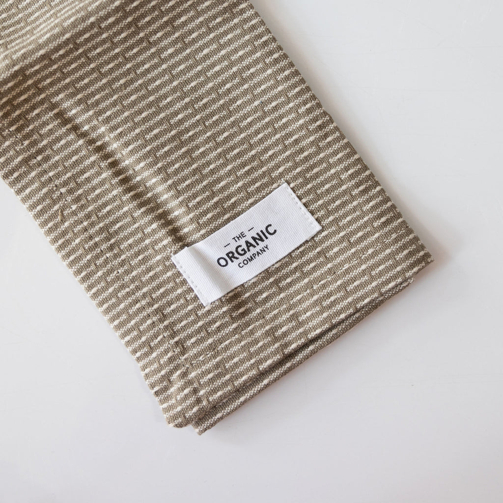 Organic cotton pique woven kitchen and washcloth folded on a white background. Tan and cream subtle striping.