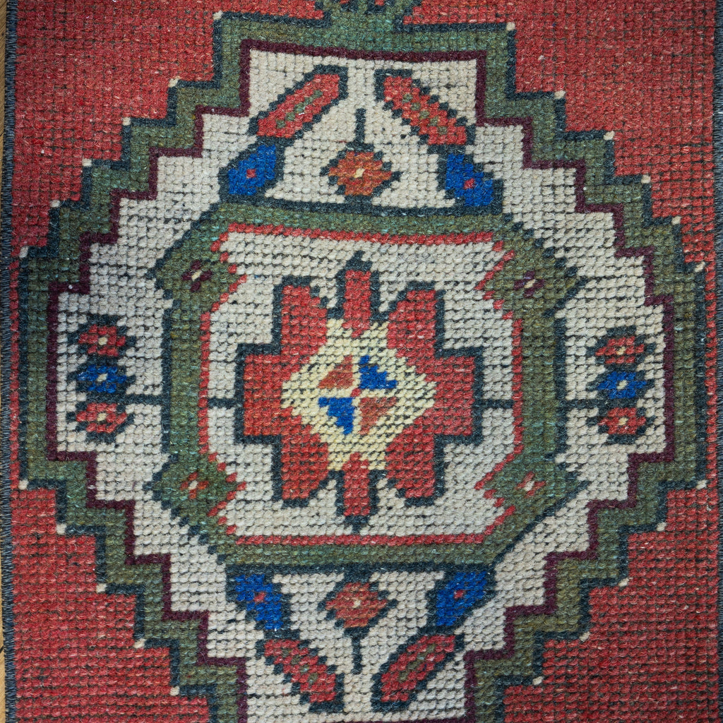 Close up of a small vintage Turkish rug with classic bold geometric design in red, green, blue, cream, maroon, and pale yellow.