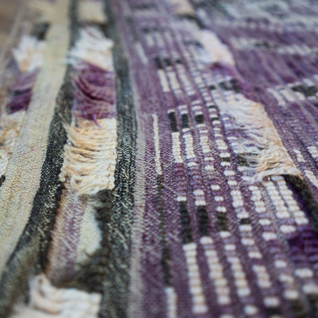 Close up of the summer side or back side of a vintage Moroccan Boujad rug with a bold geometric ombre Berber pattern featuring diamonds and zig zags in shades of purple, olive green, cream, and peach. Wood floor.