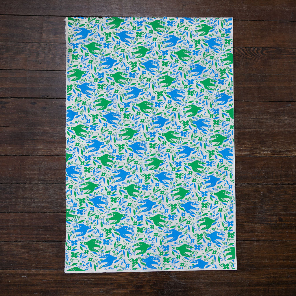 Handmade and printed paper gift wrap. Pattern is repeat blue and green doves, leaves, and flowers on cream background.