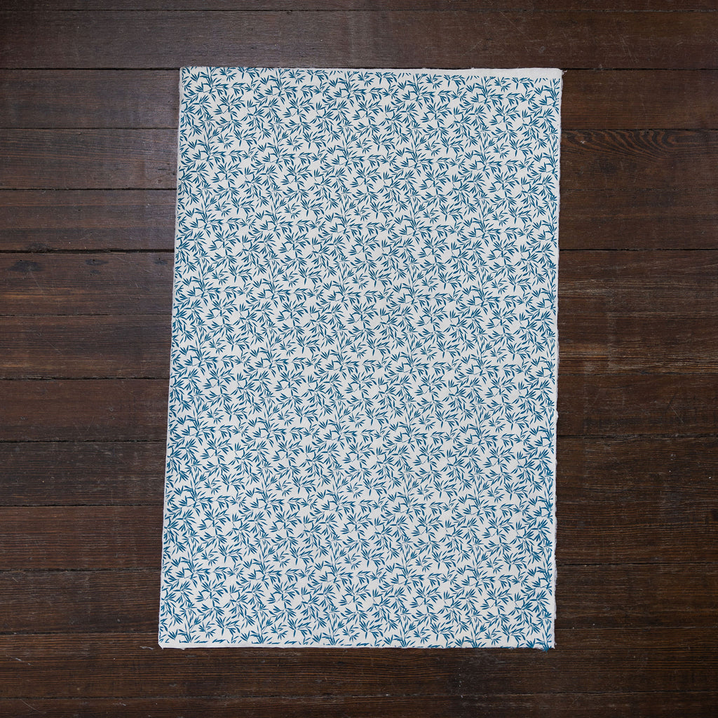 Handmade and printed paper gift wrap. Pattern is repeat teal leaves and vines on white background.