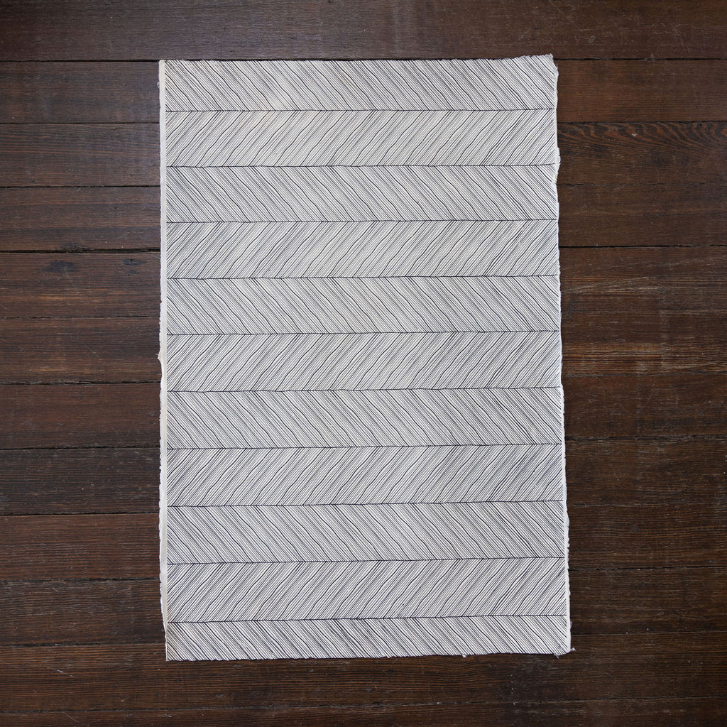 Handmade and printed paper gift wrap. Pattern is repeat dark gray herringbone on cream background.