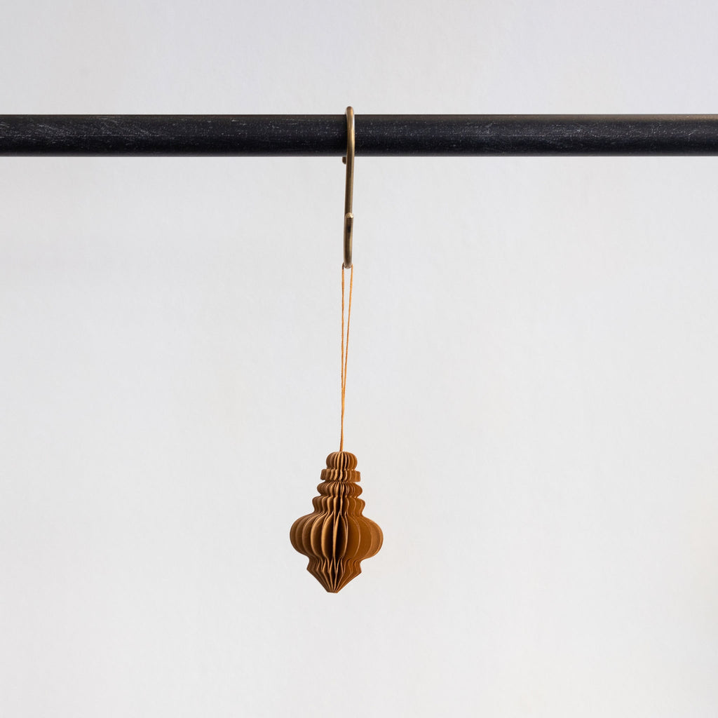 Recycled paper accordion tree ornament in Caramel hanging from a brass hook on a black bar in front of a white background.