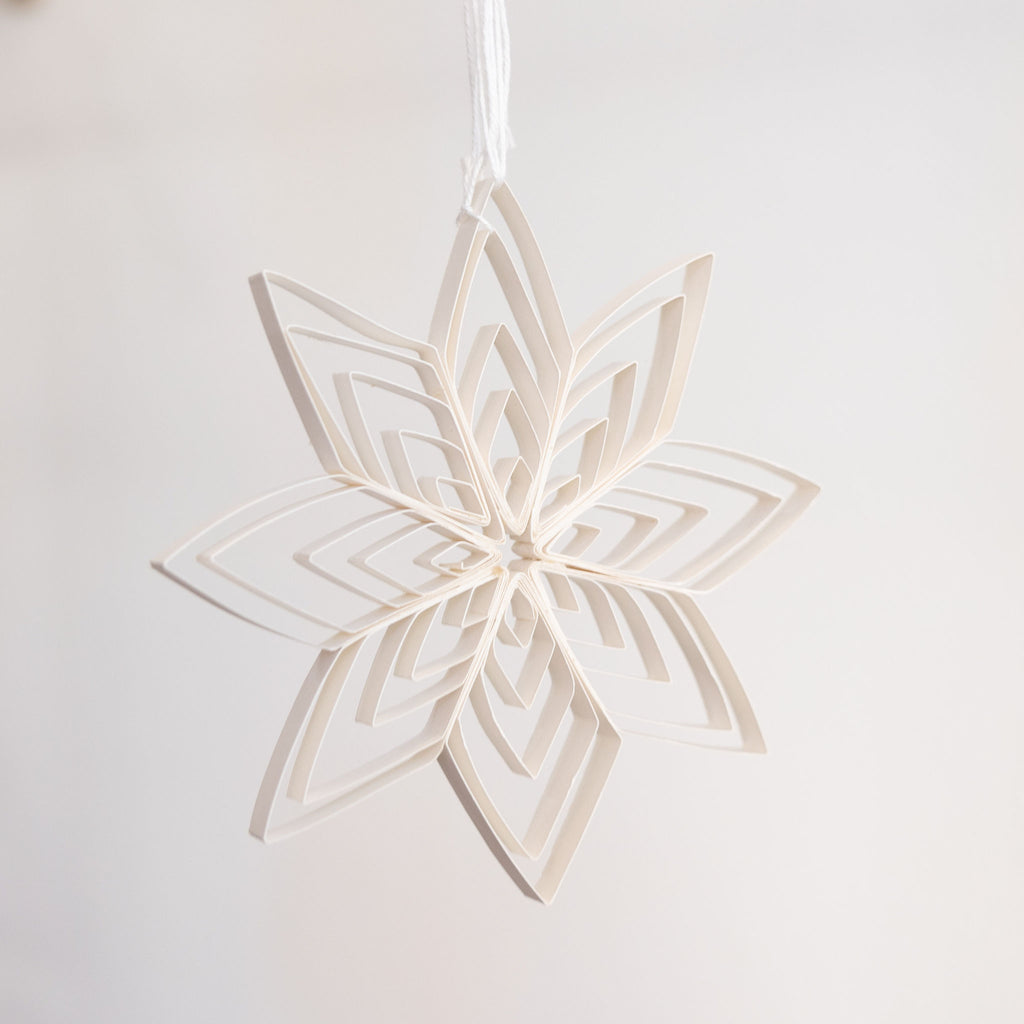 8 point radiating quilled paper start holiday decoration in white hanging in front of a light gray background.