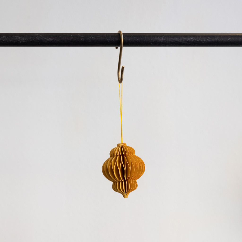 Recycled paper accordion tree ornament in Gold hanging from a brass hook on a black bar in front of a white background.