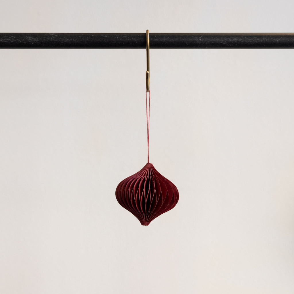 Recycled paper accordion tree ornament in Bordeaux hanging from a brass hook on a black bar in front of a white background.