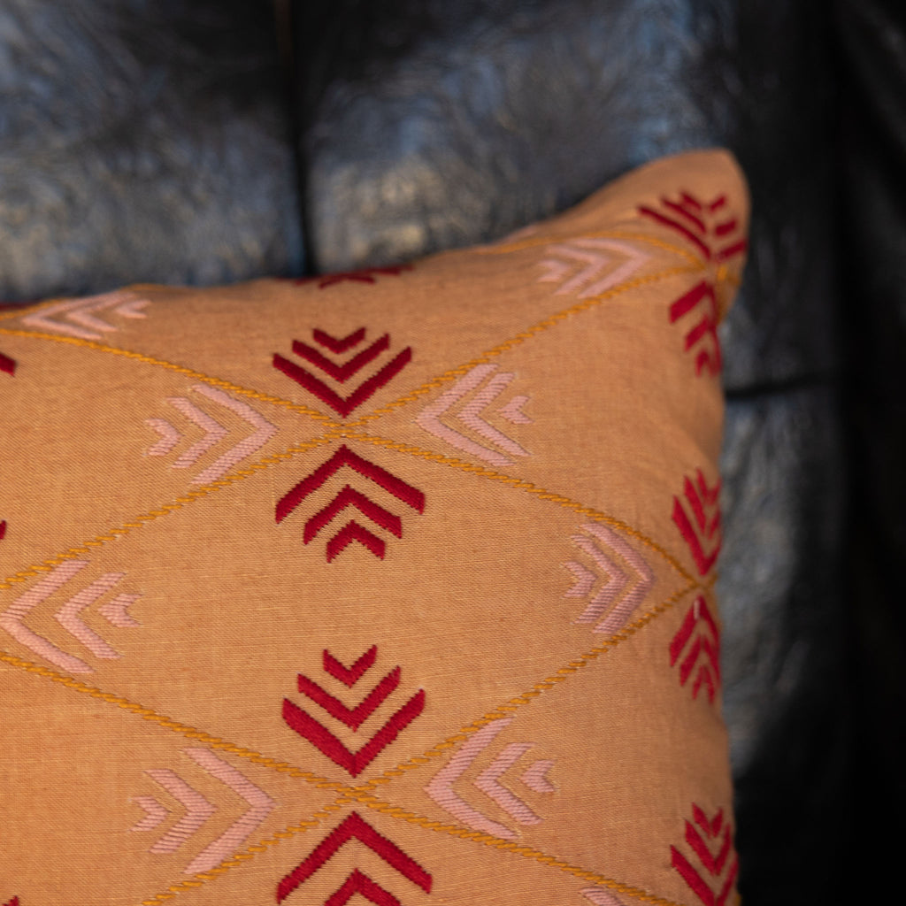 Embroidered tangerine colored lumbar pillow with red + blush pink arrow design. Close up on design.