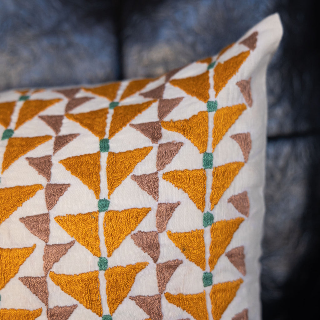 Embroidered cream lumbar pillow with mustard + mauve arrow design with green dashes. Close up.