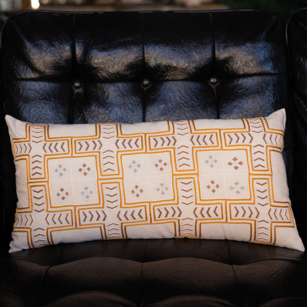Embroidered cream lumbar pillow featuring Tarshumar design embroidery, with symmetrical crosses and small arrows and small diamonds.