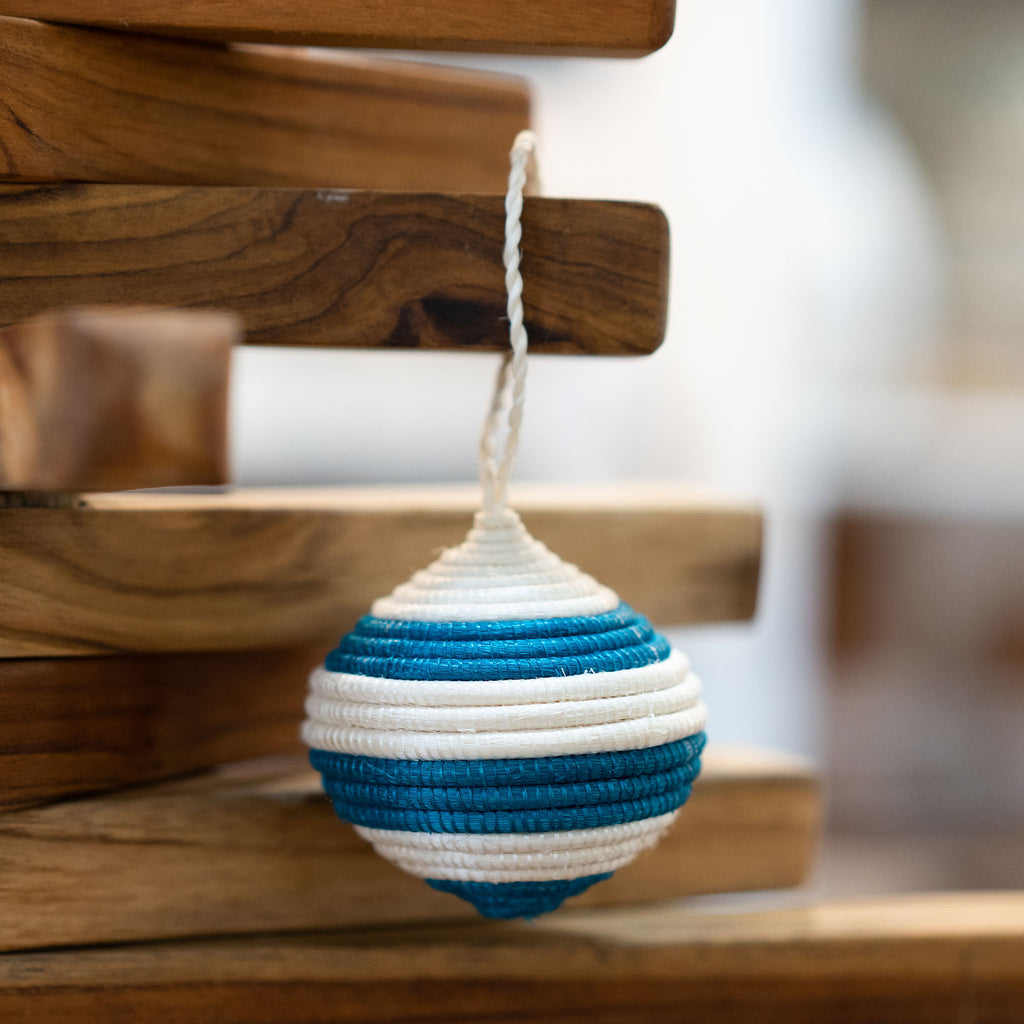 Handwoven round turquoise and white striped sweetgrass Rwandan tree ornament. Wood background