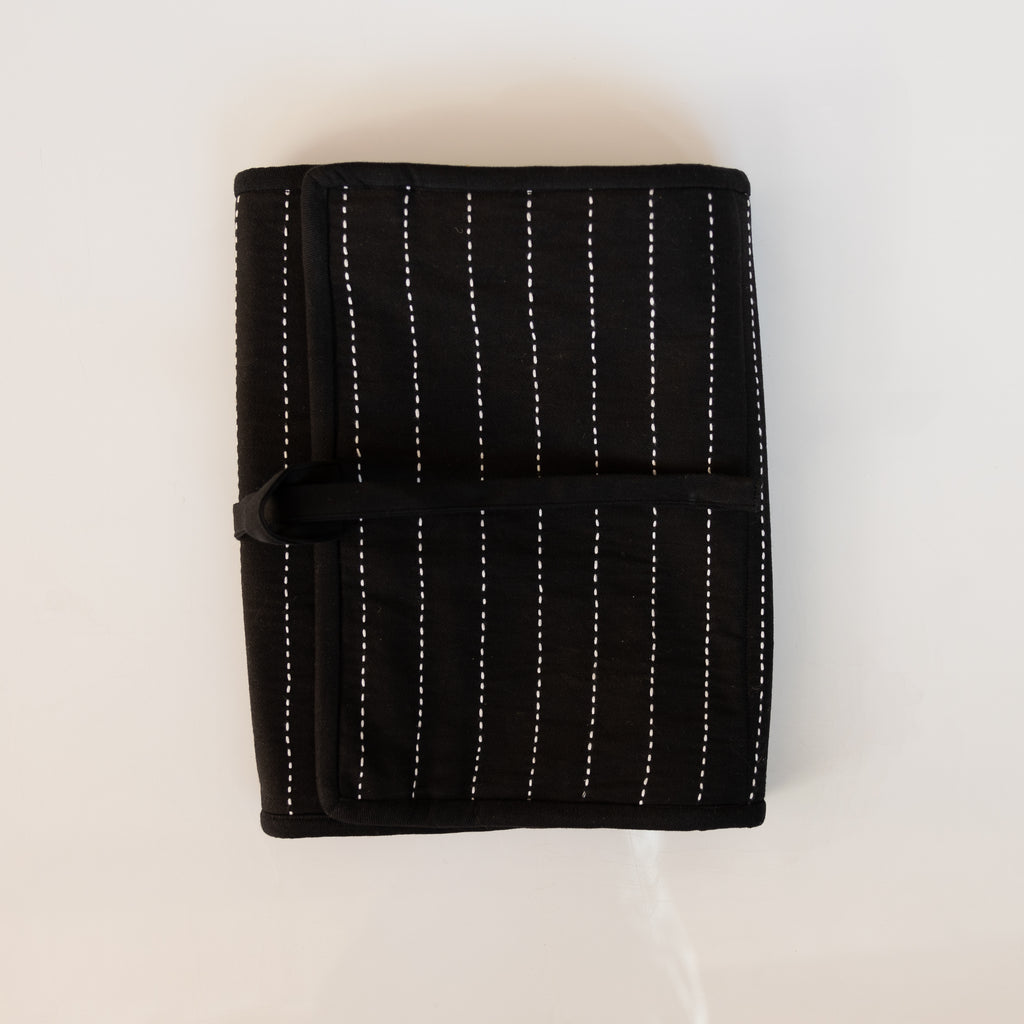 Black organic cotton hanging travel organizer embroidered with traditional kantha stitching in white folded and wrapped up to travel. White background.