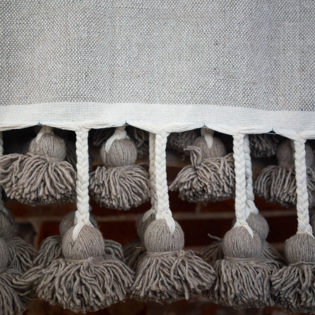 Close up of woven cotton taupe colored blanket with poms on the edge