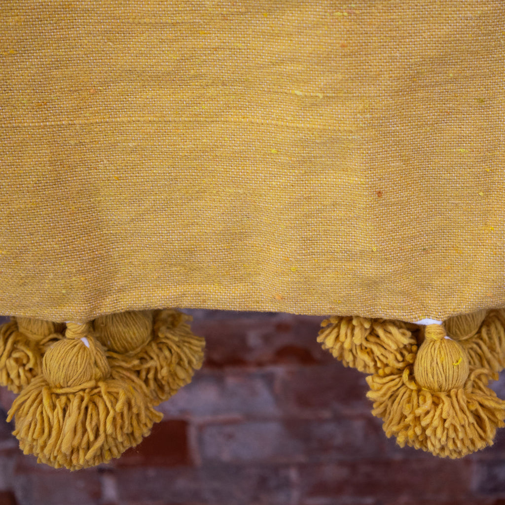 Close up of poms along the edge of mustard woven cotton blanket.