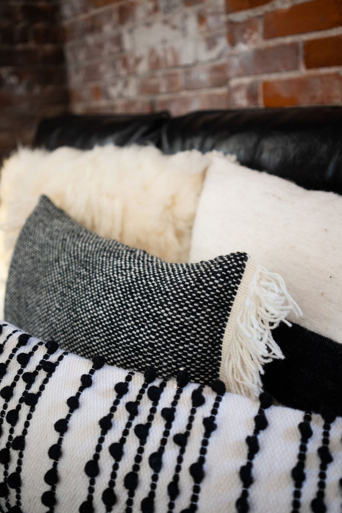 Close up on a group of four wool black and cream pillows. A lot of texture with tufts, fringe, poms, sheep wool.