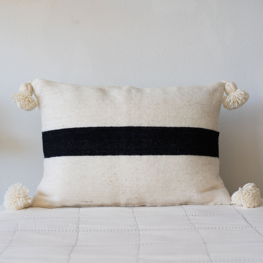 Large cream rectangle wool pillow with a wide black stripe woven through the center horizontally. Cream poms at each corner.