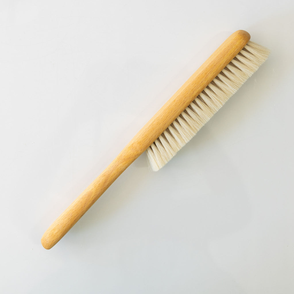Side of a slim dust brush made from goat hair and beechwood.