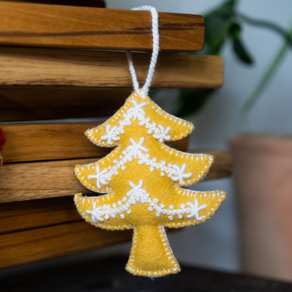 Wool Christmas tree ornament in the shape of a Christmas tree. Mustard with cream embroidery. Wood background.