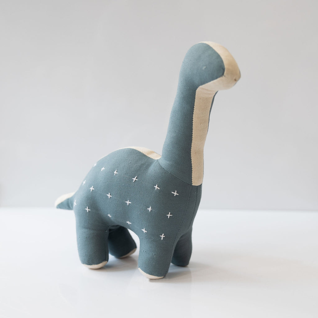 A handmade and kantha stitched stuffed dinosaur in cream and blue gray color way. Sitting in front of a white background.