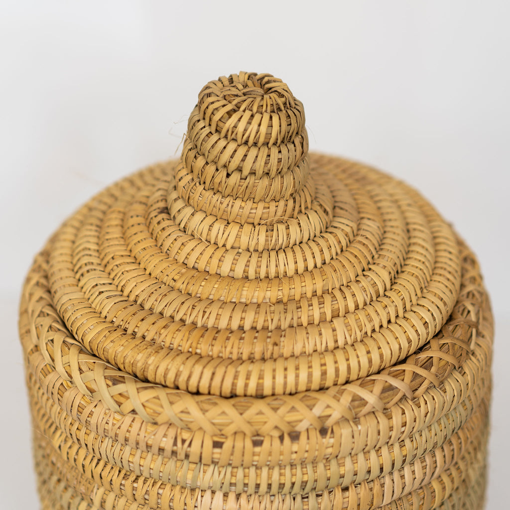 Detail shot of knob handled lid of small rush fiber handwoven basket. Light gray background.