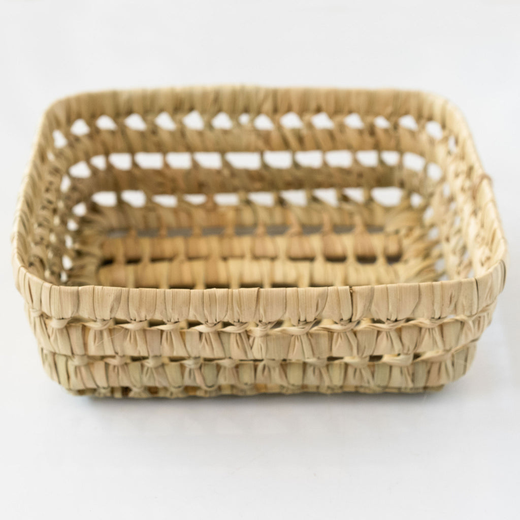 Palm fiber loosely woven rigid basket sits against a white background.