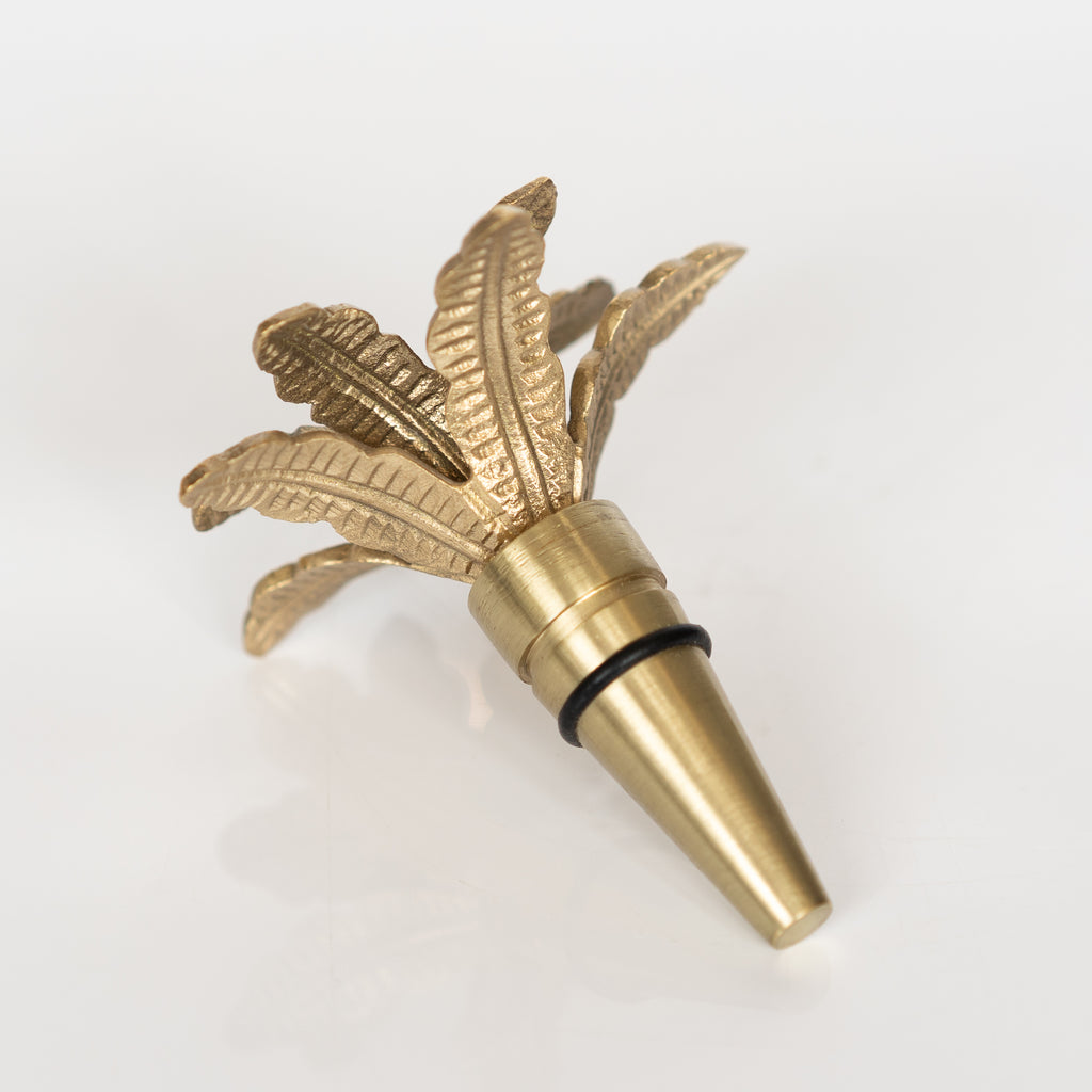 Recycled brass bottle stopper in a palm tree design with two rows of palm fronds on top. Light gray background.