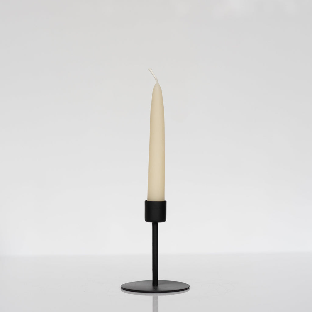 Medium height modern matte black taper candle holder holding an ivory taper candle.