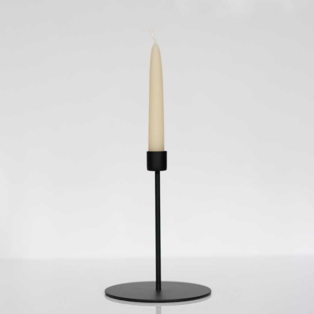 Tall modern matte black taper candle holder holding an ivory taper candle.