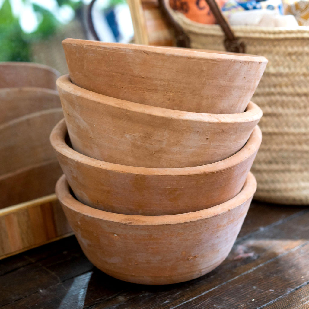A stack of smaller round and low terra cotta plant pots sitting in front of a basket on a wood floor.
