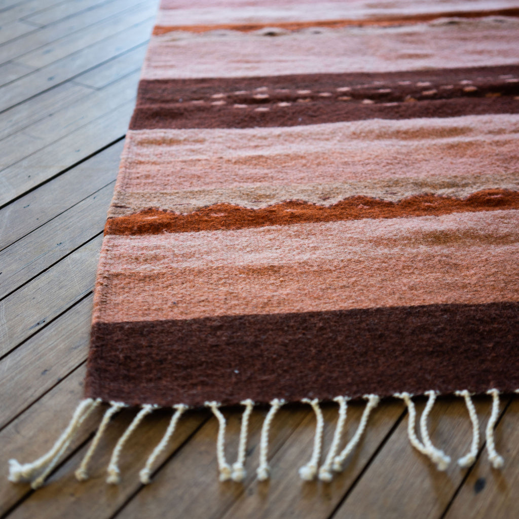 Close up of the fringed corner of a flat woven wool Oaxacan rug with traditional Oaxacan designed stripes. Wood floor.