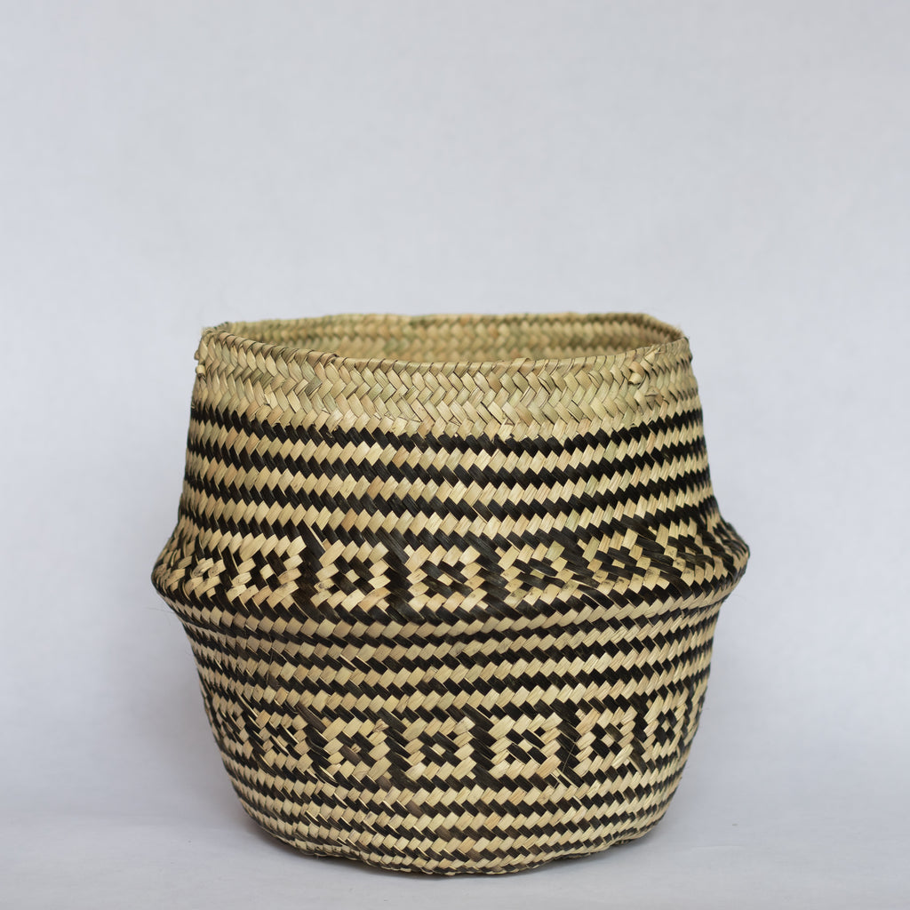 Handwoven palm fiber belly basket in traditional Oaxacan designs. Tan and black stripes alternate with rows of contrasting layered squares. Gray background. 
