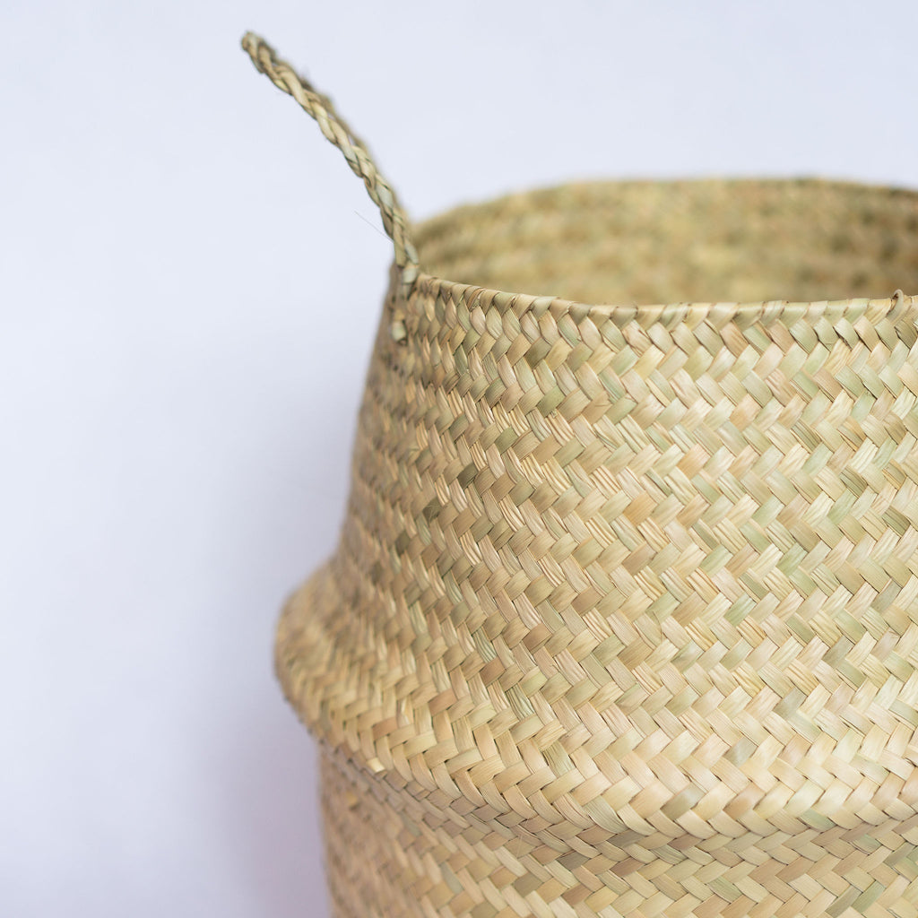 Close up of handwoven palm fiber belly basket with handles in natural tan. Gray background.
