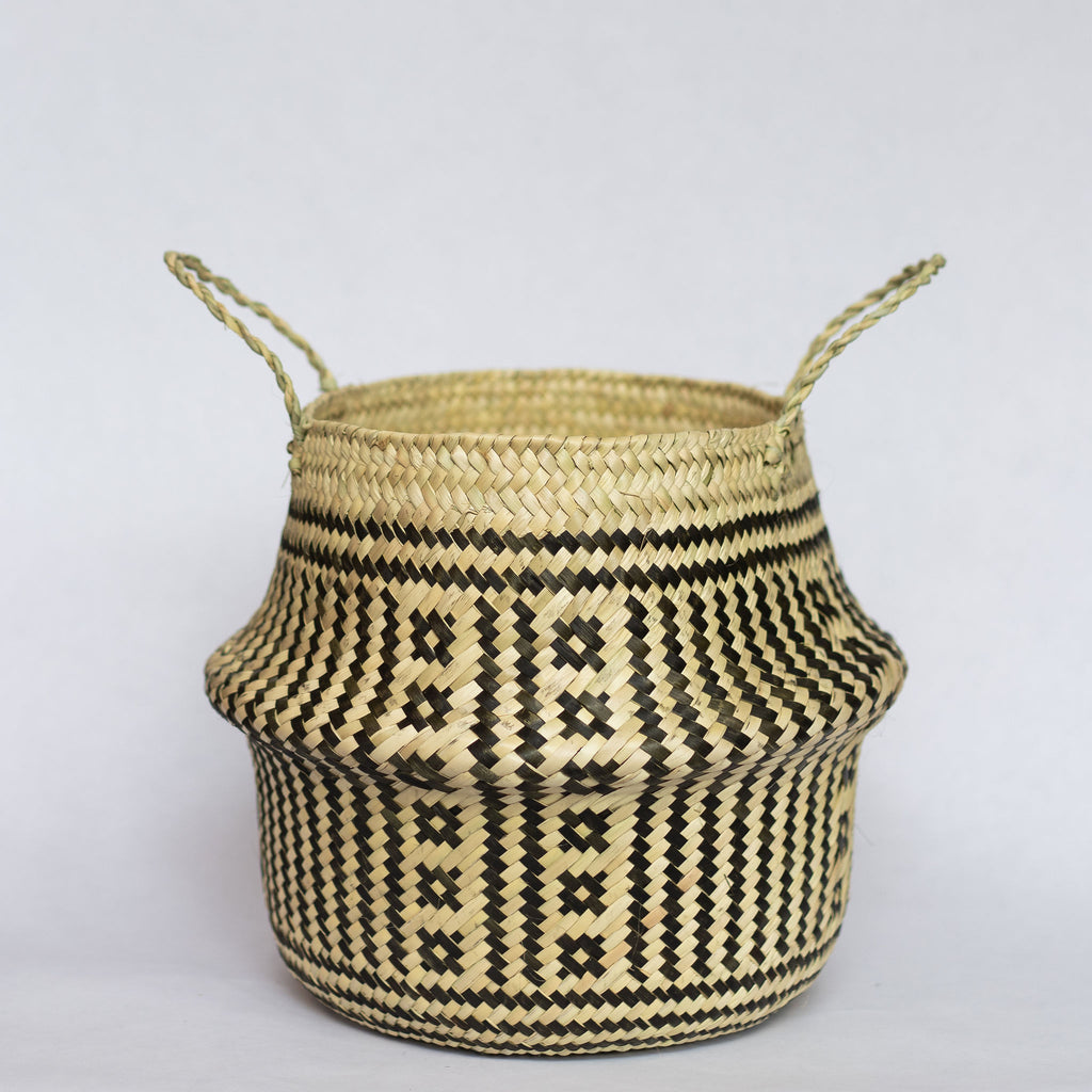 Handwoven palm fiber belly basket with handles in traditional Oaxacan designs. Tan and black vertical stripes alternate with two vertical rows of small squares in each quarter of the basket.  Horizontal stripes run along both top and bottom edge. Gray background.