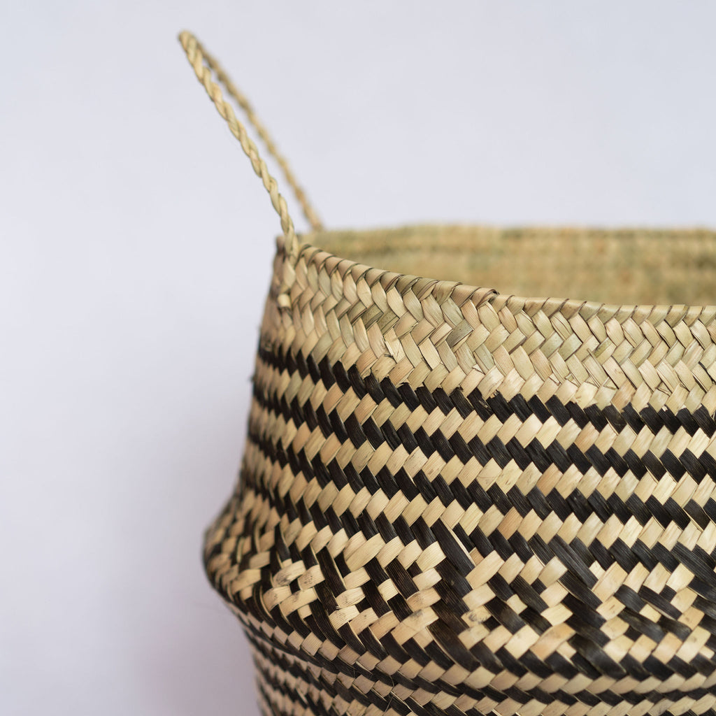 Close up of handle of handwoven palm fiber belly basket in traditional Oaxacan designs. Tan and black stripes alternate with rows of contrasting layered squares. Gray background.